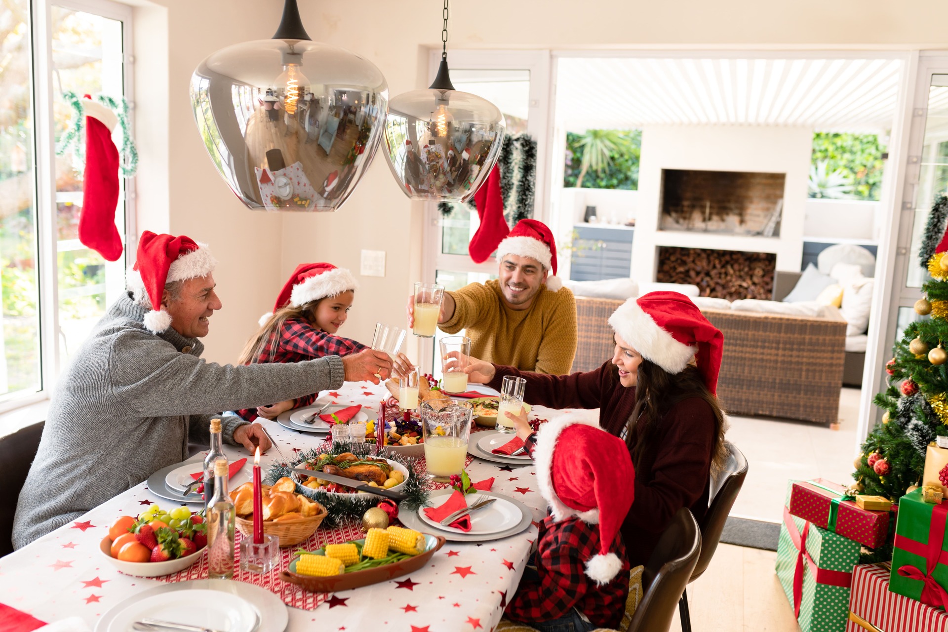 Famille multigénérationnelle caucasienne portant des bonnets de père Noël en train de prendre un repas de Noël.