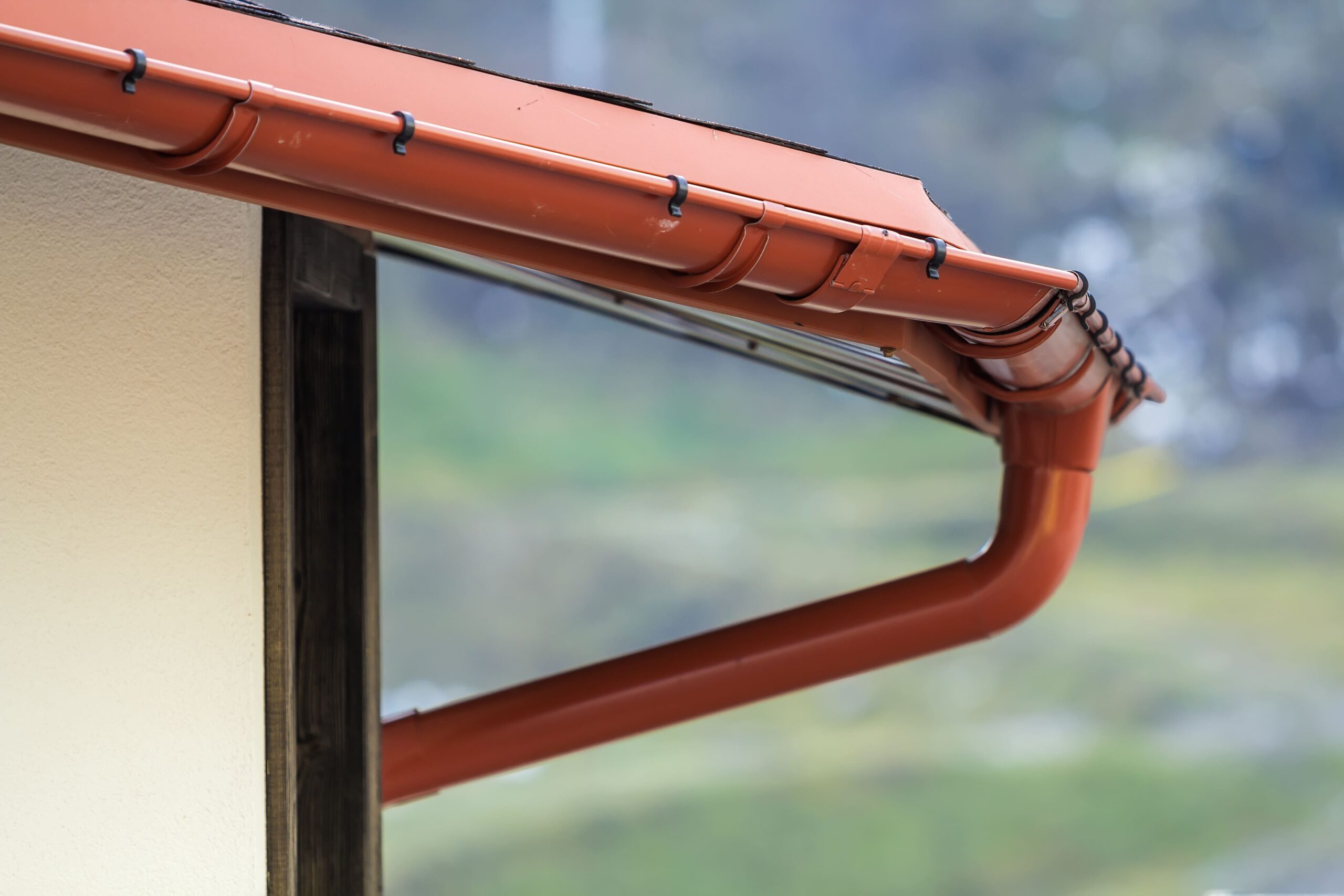 Installation de gouttière en PVC rouge-brun avec descente d'eau pluviale sur façade de maison