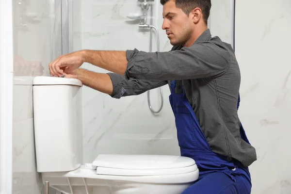 Plombier professionnel en Belgique effectuant le remplacement d'un WC dans une salle de bain moderne. Il porte un uniforme de travail bleu et travaille avec soin pour garantir un système de plomberie fiable.