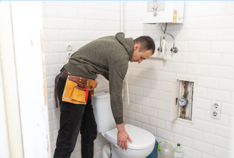 Homme devant des toilettes, ventouse et plomberie visibles, prêt à intervenir pour déboucher une canalisations wc avec outils professionnels. déboucheur wc